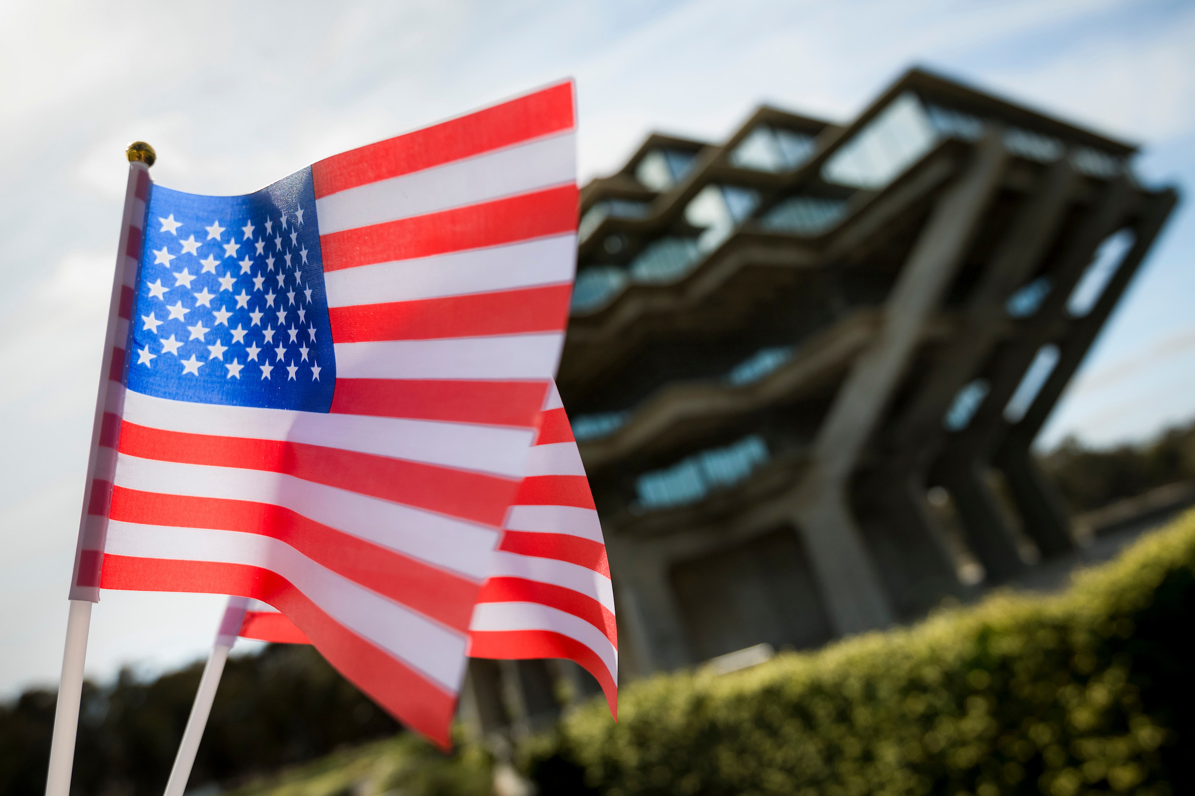 Two American flags wave in breeze in front of Geisel Library.