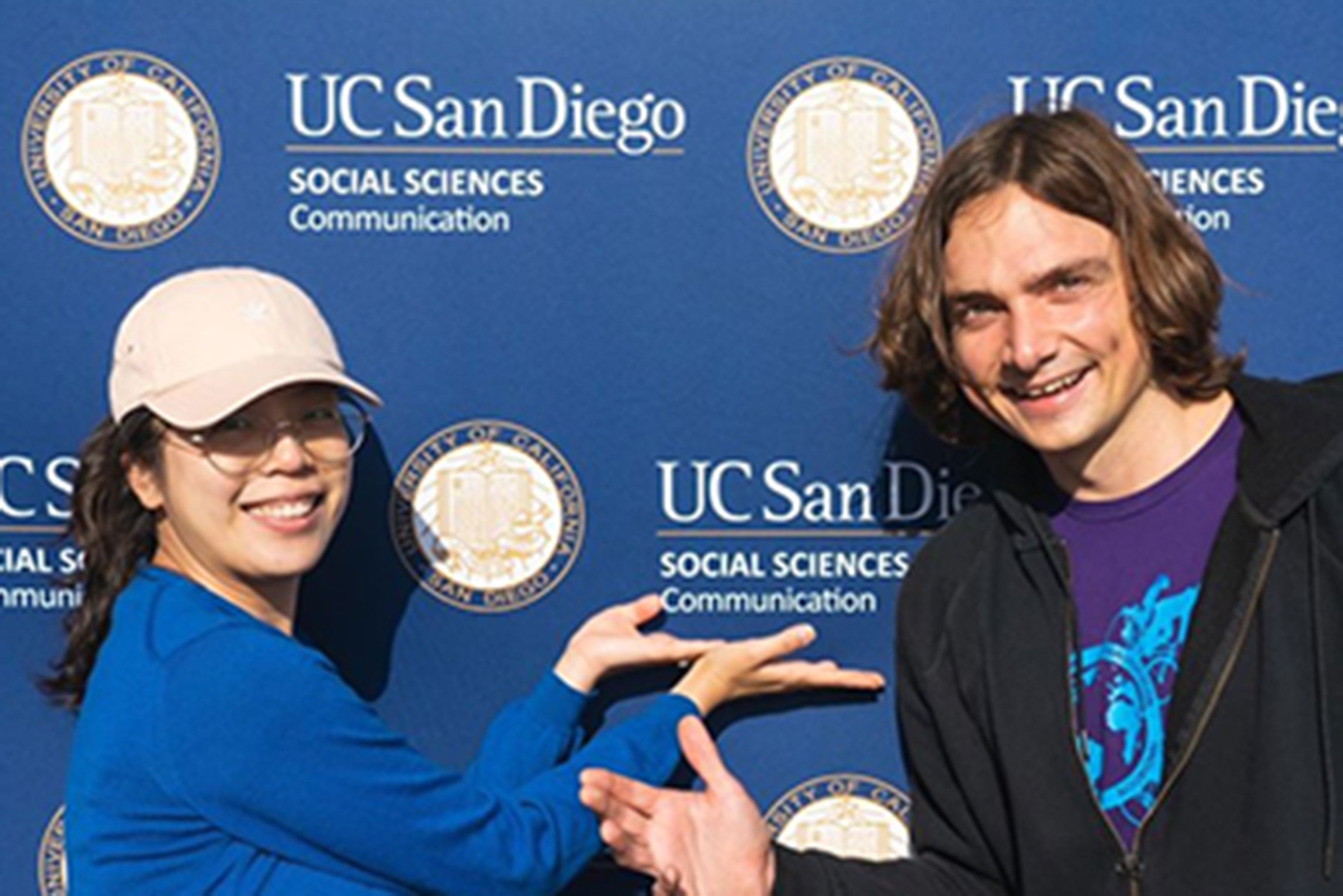 Two students point at backdrop that reads "UC San Diego Social Sciences Communication