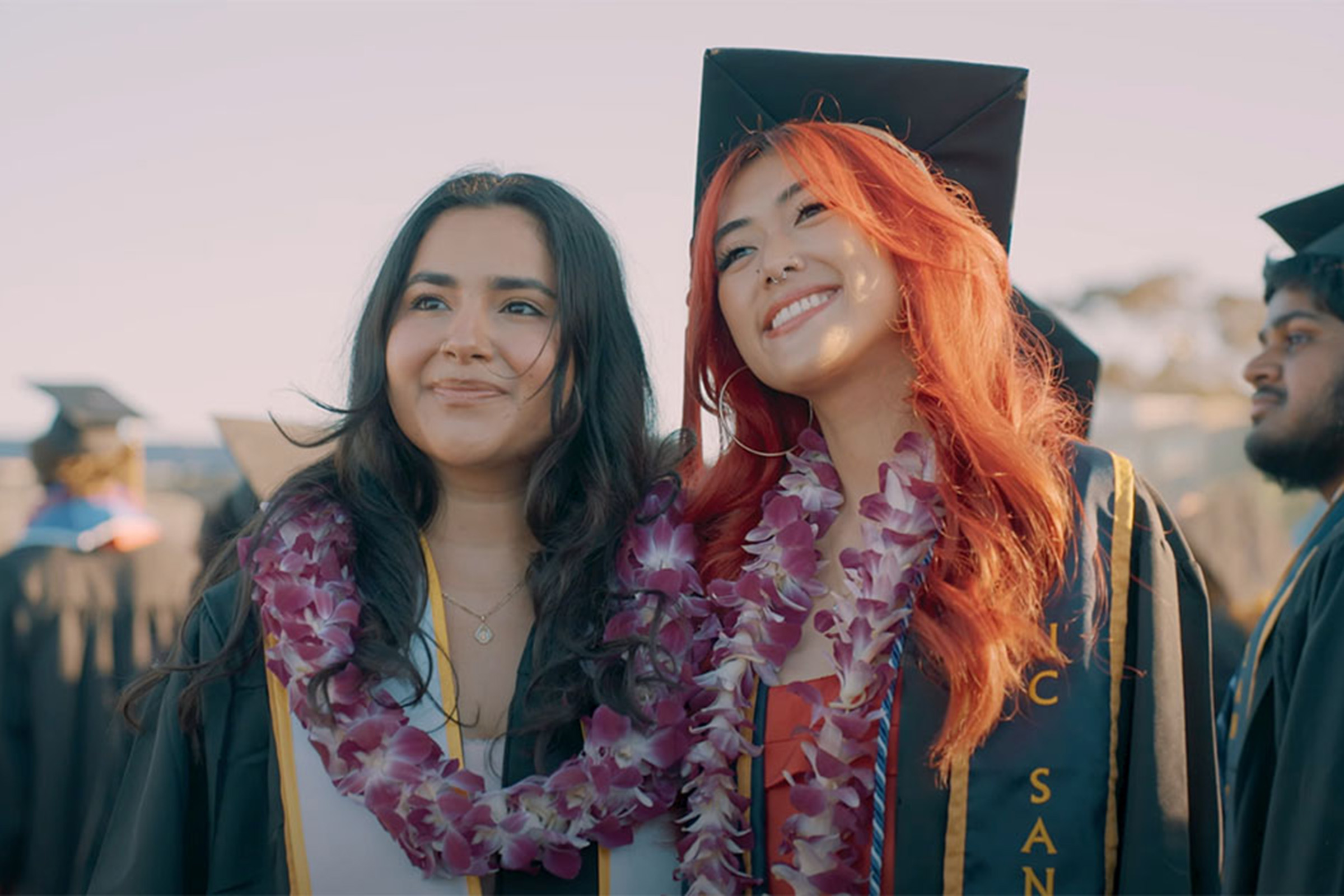 Two graduates wearing floral leis pose for photo